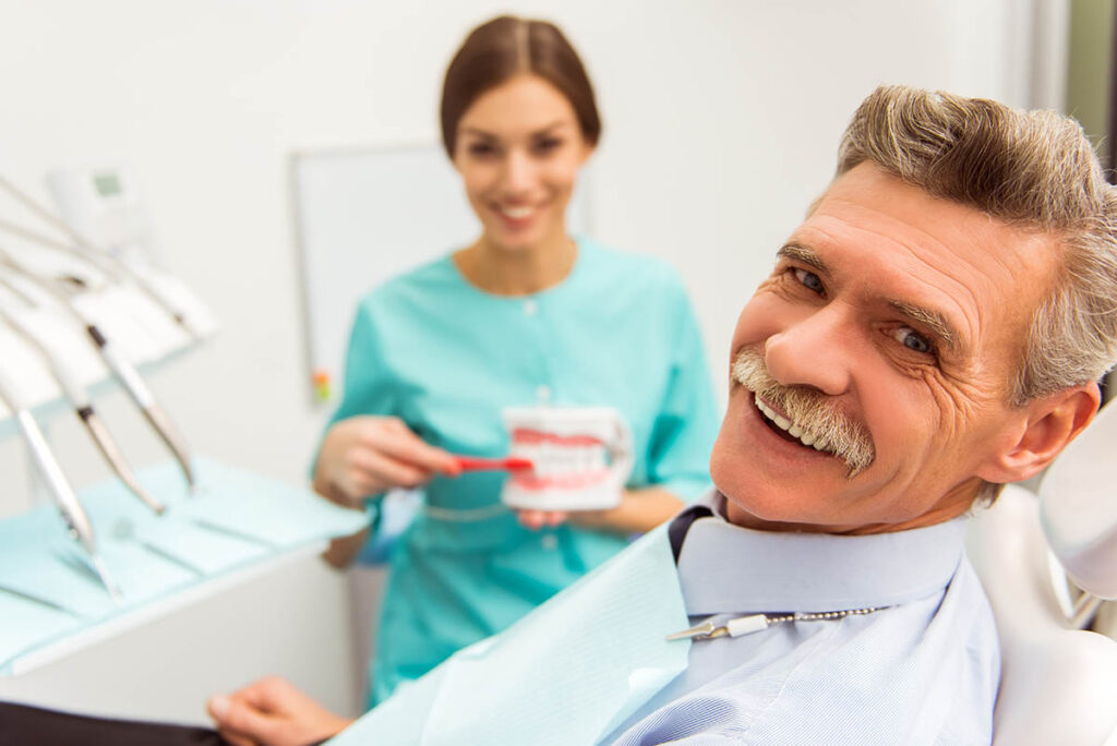 man looks at camera with dentist in frame discussing the dental bridge recovery time