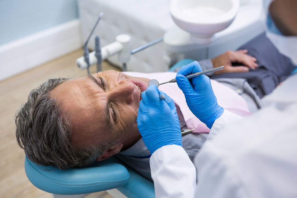 patient sits in a dental exam chair while dentist works on their teeth and explains the many flipper and removable partial denture benefits