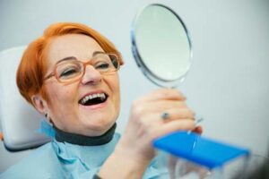 woman looks in the mirror at her implant-retained dentures