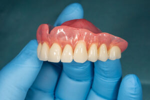 dentist wearing blue gloves and holding dentures to show the difference between dental implant overdentures vs. traditional dentures