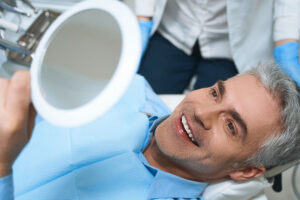 person smiling into mirror after receiving dental implants near cary nc