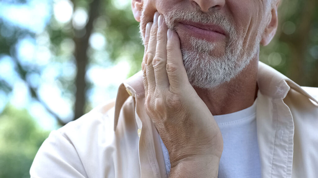 person touching sore jaw while struggling with poor dental health