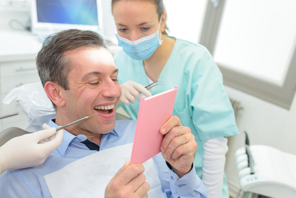 person happy while looking in mirror after covering cost of dental bridges for a new smile