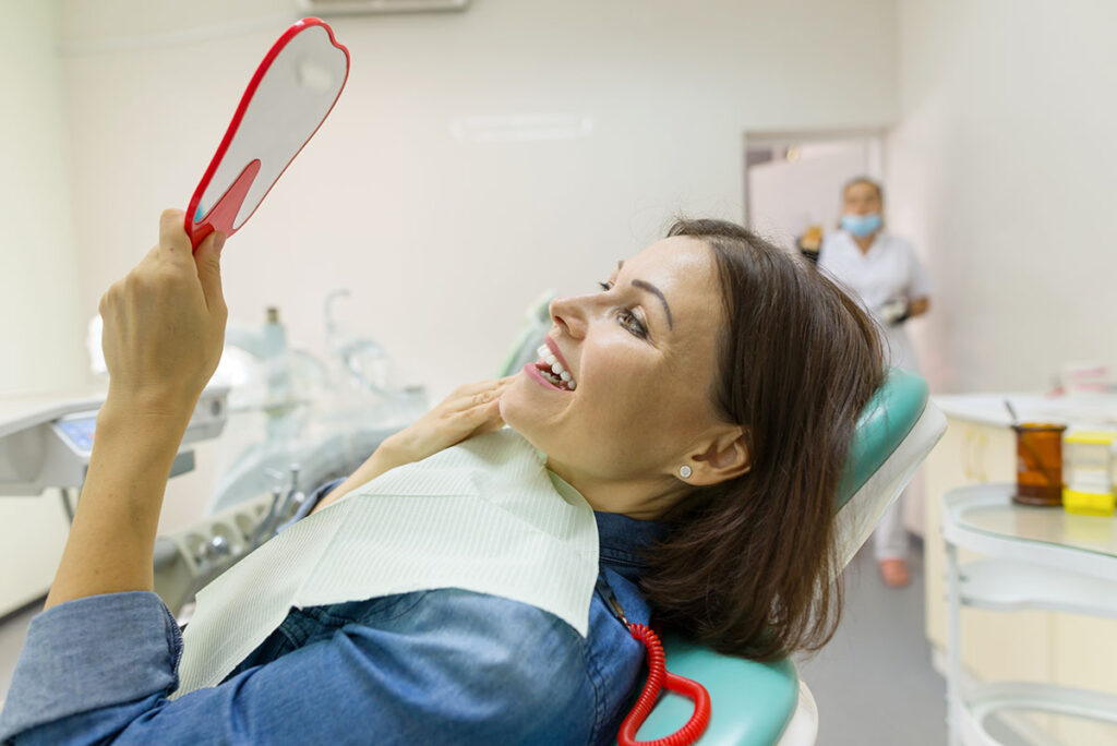 person in dental office looking at new smile in mirror and asking how long do dental implants last