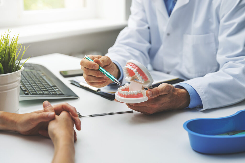 dentist holding model of teeth while explaining why would a general dentist refer a patient to a prosthodontist