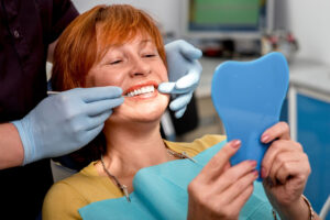 person smiling in handheld mirror after investing in digital dentistry