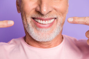person smiling and pointing at teeth after dental implant maintenance