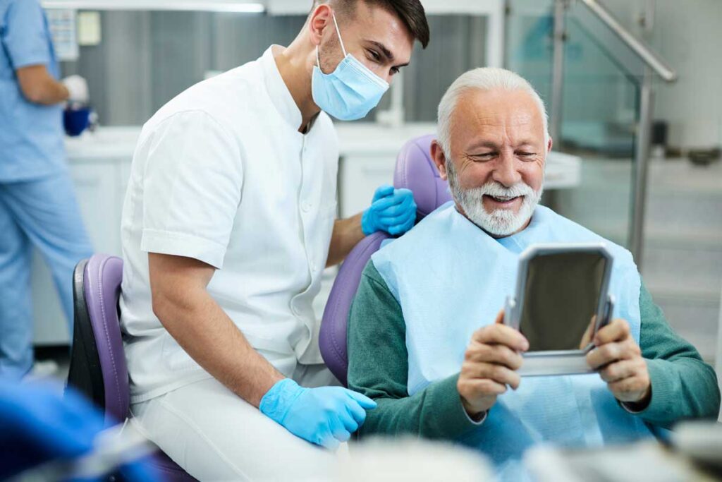 a man in a dentist's office smiles with a tech after getting his dental implants restored
