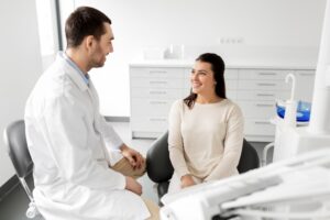 A dentist in a white coat talks with a patient seated in a dental chair, discussing treatment options in a bright, clean clinic setting.